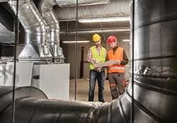 Technicians with red and yellow hard hats inspecting commercial HVAC ducting